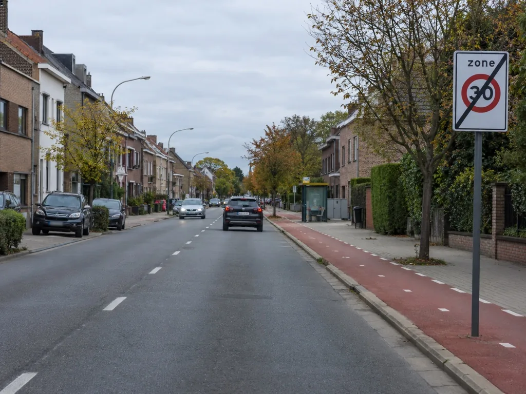 Straat in een bebouwde kom met een rood fietspad rechts en een bushalte verderop.