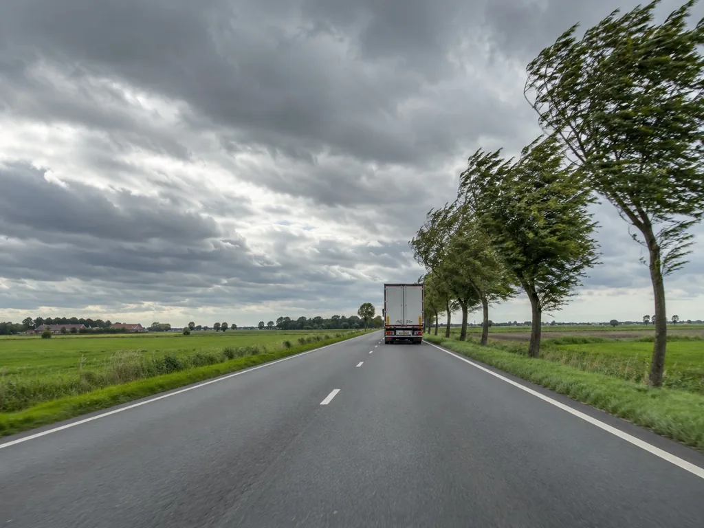 Een vrachtwagen rijdt voor u op een open, winderige weg.