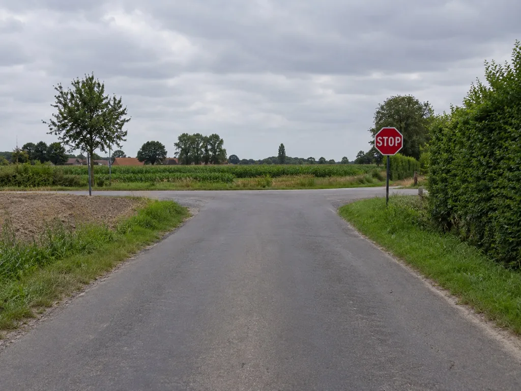 Landelijk kruispunt met een rood achthoekig stopbord aan de rand van de rijbaan, zonder stopstreep op het wegdek.